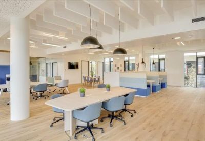 Open-plan coworking space with long tables, blue seating, and hanging light fixtures.