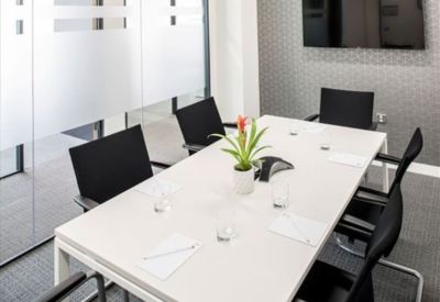 Modern meeting room with a white table, black chairs, and a wall-mounted television.