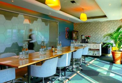Long wooden boardroom table with modern grey chairs and bright yellow pendant lights.