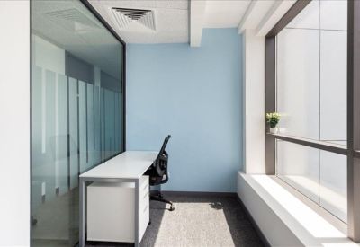 Private glass-walled office with a white desk and light blue feature wall.