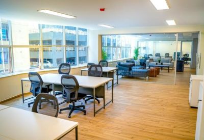Open-plan office with white desks and ergonomic black chairs near a window.
