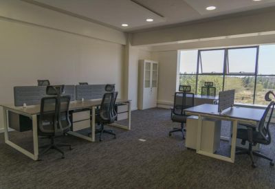 Open-plan office space with multiple workstations, ergonomic chairs, and large windows.