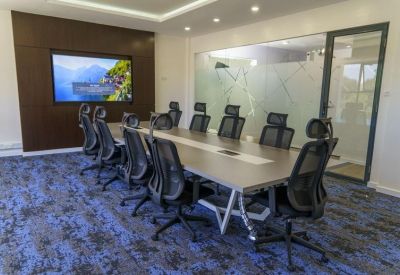 Professional boardroom with a long table, ergonomic mesh chairs, and a wall-mounted screen.