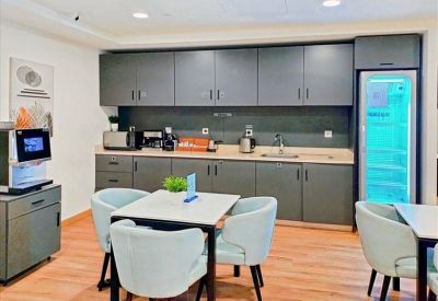 Modern office kitchen with grey cabinetry, coffee machine, and dining area.