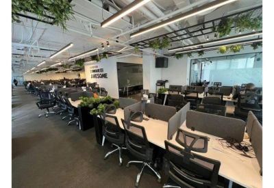 Modern coworking area with partitioned workstations and indoor plants under linear lighting.