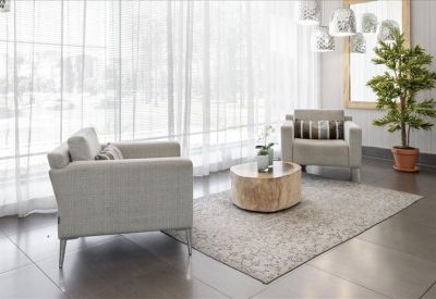 Lounge area with comfortable armchairs and a small round wooden table by a sheer window.