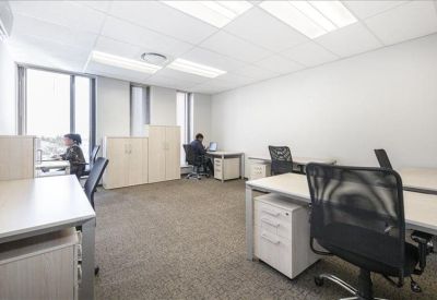 Brightly lit shared office suite with several desks, ergonomic chairs, and large windows.