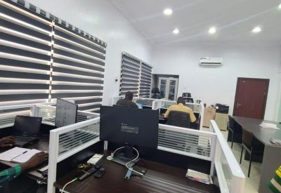 Open-plan office space featuring several cubicle workstations with dark wood desks and privacy dividers.