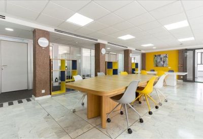 Modern coworking space with a large wooden table and yellow accent chairs.