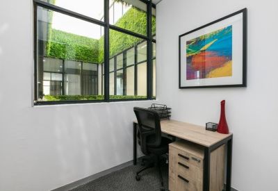 Private office with a light wood desk, ergonomic chair, and a view into a green courtyard.