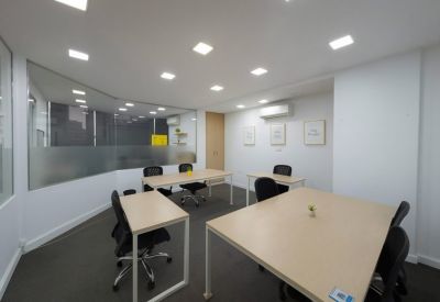 Spacious open-plan office with multiple light wood desks and recessed ceiling lights.