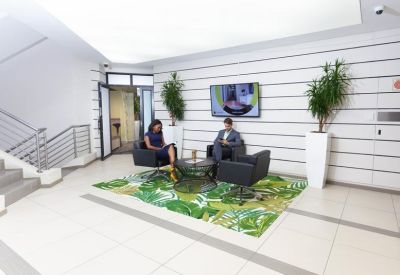 Lobby area with a leafy green rug and two people in armchairs.