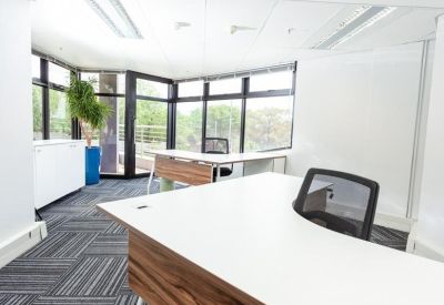 Corner office suite with wood-finish desks and large windows.