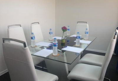 Meeting room with a glass table, white modern chairs, and complimentary water bottles.