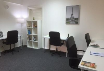 Coworking area with several white desks, black chairs, a bookshelf, and Eiffel Tower wall art.