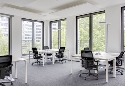 Modern workspace with multiple white desks and ergonomic black chairs near large windows with leafy views.