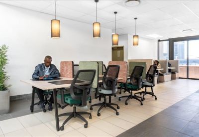 Open-plan coworking area with rows of desks, mesh chairs, and warm pendant lighting.