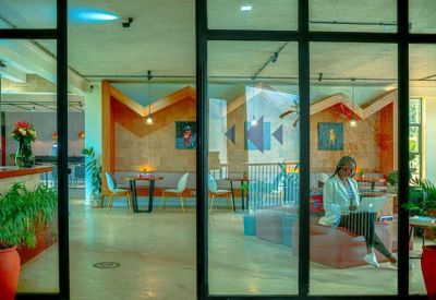View through glass doors into a vibrant communal area with colorful seating and potted plants.