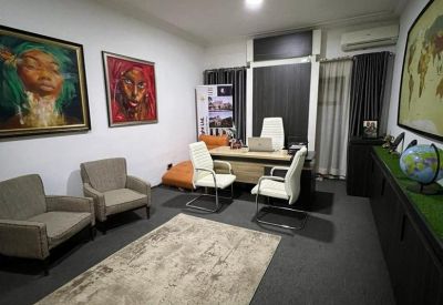 Private office suite with a wood-toned desk, white leather chairs, and large framed artwork.