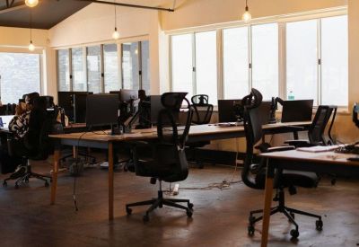 Open-plan office with multiple rows of workstations and ergonomic black mesh chairs.