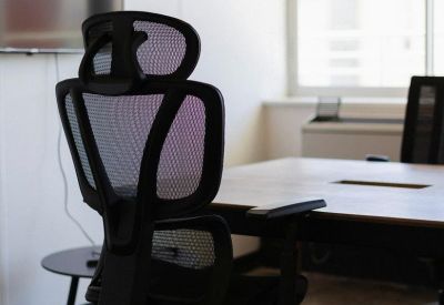Modern black mesh office chair in a bright meeting room with a large wall-mounted screen.