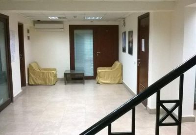 Waiting area or corridor featuring two yellow armchairs and glass-walled office partitions.