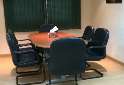 Meeting room with an oval wooden table, black ergonomic chairs, and dark green blinds.