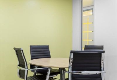 Small meeting room with a round wooden table, four black leather chairs, and lime green wall.
