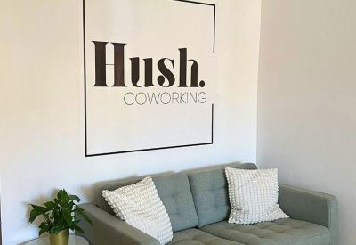 Reception lounge with a light green sofa, potted plant, and branded wall signage.