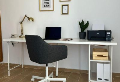 Single workstation desk with a laptop, black chair, and framed wall art.