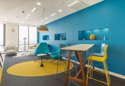 Bright breakout space with a vibrant teal feature wall, yellow stools, and a yellow rug.