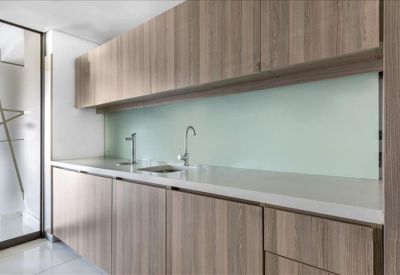Sleek office kitchenette with light wood cabinetry and minimalist white countertops.