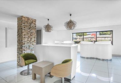 Contemporary reception lobby with stone feature pillar, white counters, and green armchairs.
