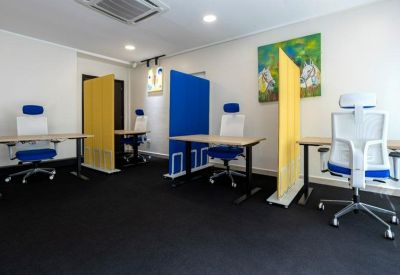 Modern coworking space with blue and yellow acoustic dividers and ergonomic white and blue chairs.