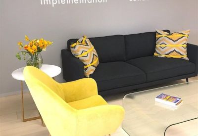 Lounge area with a yellow armchair, black sofa, and motivational wall decals.