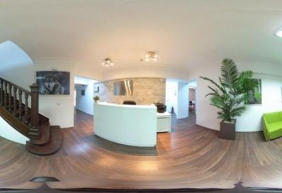 Spacious reception lobby with a curved white desk, wooden floors, and vibrant green seating area.