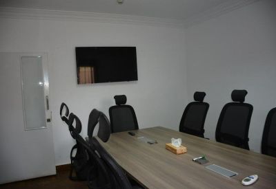 Contemporary meeting room with a large rectangular table, wall-mounted screen, and black chairs.