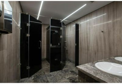 Modern restroom with dark marble-style tiling, black stall doors, and circular white sinks.
