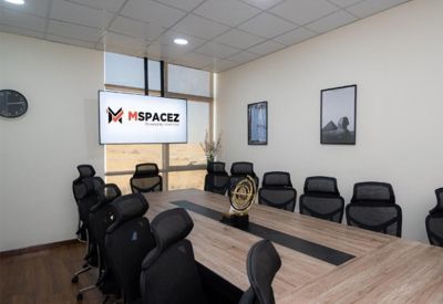 Spacious meeting room with a large wooden table, black mesh chairs, and a wall-mounted screen.