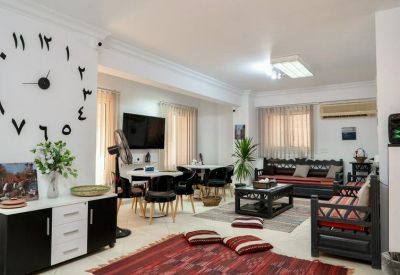 Spacious communal lounge featuring a large wall clock, dining area, and traditional wooden seating with red cushions.