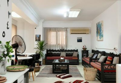 Bright living area with dark wood sofas, striped cushions, a central coffee table, and large window with light curtains.