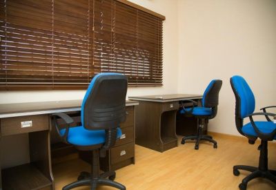 Private office with two dark wood desks, blue rolling chairs, and wooden window blinds.