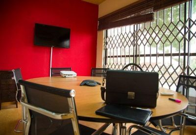 Meeting room featuring a red accent wall, large oval wooden table, and window with security bars.