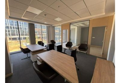 Bright open-plan office with wooden desks and large windows overlooking other buildings.