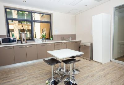 Modern office kitchen with a tall white cabinet and a square breakfast table with stools.