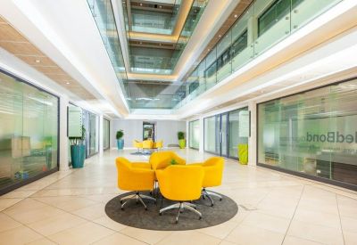 Bright glass-walled lobby with yellow bucket chairs and an atrium ceiling.