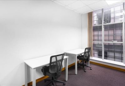 Bright two-person office suite featuring white desks and black mesh chairs near a large window.
