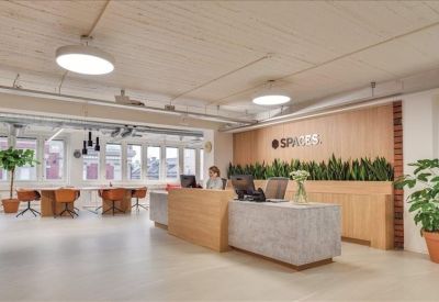 Modern wooden reception desk with greenery and a seating area in the background.