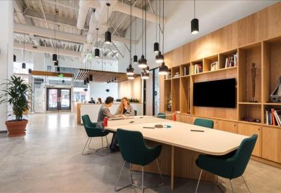 Bright conference room with a long wooden table, teal chairs, and a large display screen.
