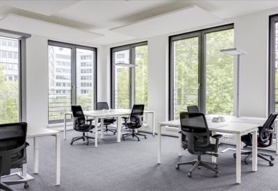 Bright open-plan office with white desks, black mesh chairs, and large windows.